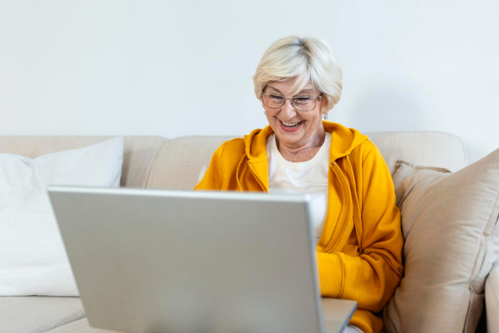 dame de 70 ans souriante qui sauvegarde ses photos facebook sur son pc